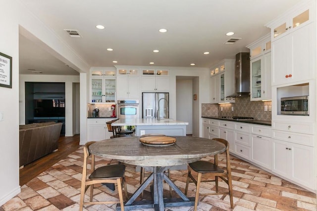 kitchen featuring visible vents, glass insert cabinets, recessed lighting, appliances with stainless steel finishes, and wall chimney exhaust hood