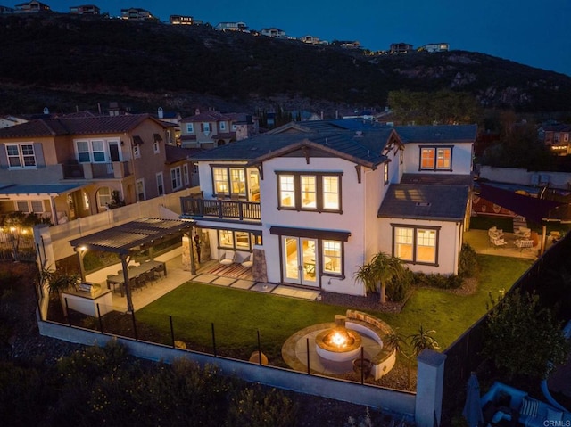 back of house at twilight with a fenced backyard, a lawn, a fire pit, and a patio