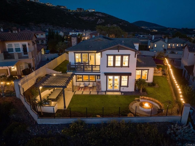 back of house at night featuring a lawn, a patio, a fenced backyard, a fire pit, and a chimney