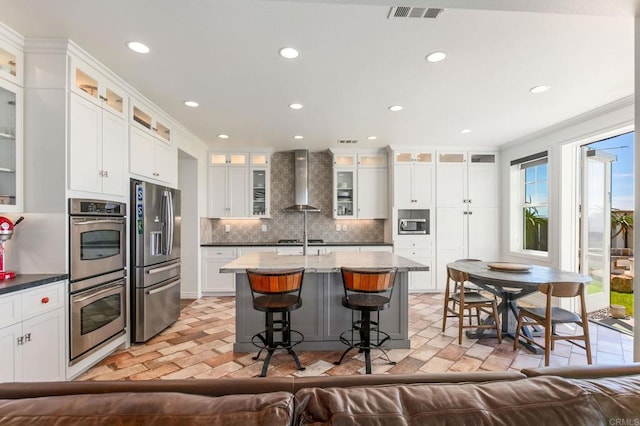 kitchen featuring visible vents, backsplash, wall chimney range hood, ornamental molding, and stainless steel appliances