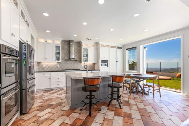 kitchen with ornamental molding, backsplash, recessed lighting, stainless steel appliances, and wall chimney range hood