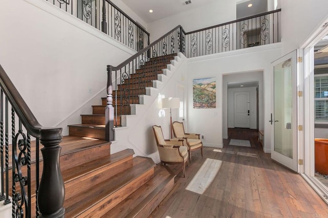 staircase featuring hardwood / wood-style floors, visible vents, baseboards, recessed lighting, and a towering ceiling