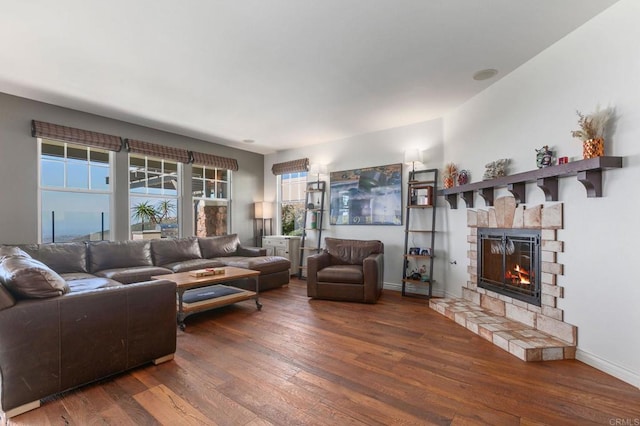 living room with a stone fireplace, baseboards, and wood-type flooring