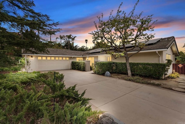 ranch-style house with a garage, concrete driveway, a tiled roof, and solar panels