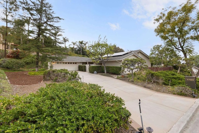 view of front facade with a garage, solar panels, fence, and concrete driveway