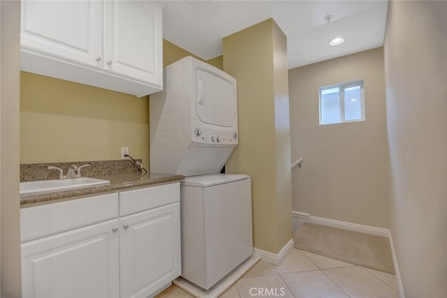 clothes washing area with light tile patterned floors, stacked washer and dryer, cabinet space, a sink, and baseboards