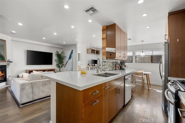 kitchen with visible vents, appliances with stainless steel finishes, open floor plan, a sink, and a warm lit fireplace