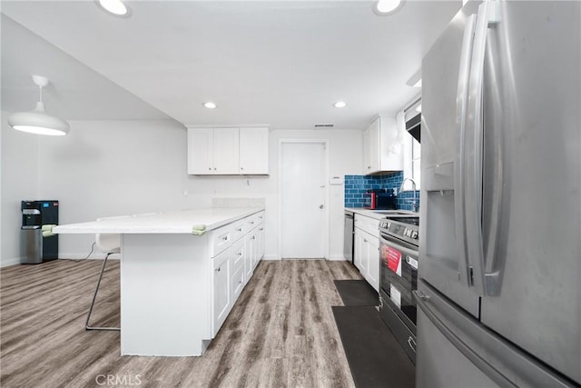 kitchen featuring a peninsula, appliances with stainless steel finishes, a breakfast bar area, and light wood-style floors