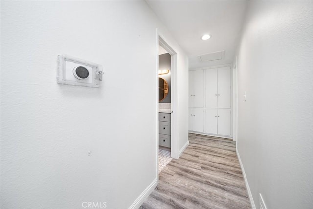 hallway featuring light wood-style flooring, baseboards, attic access, and recessed lighting