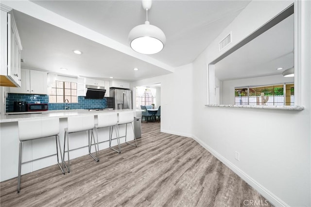 kitchen featuring visible vents, stainless steel fridge with ice dispenser, a breakfast bar area, a healthy amount of sunlight, and backsplash