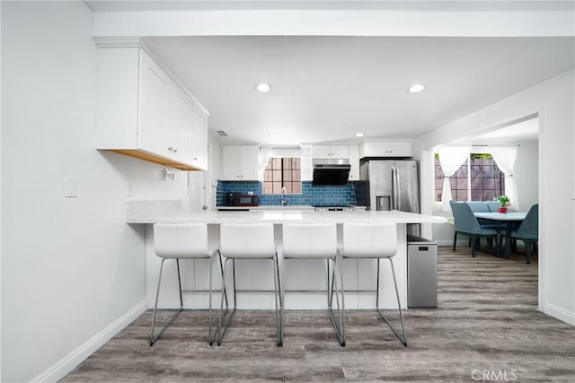 kitchen featuring a peninsula, wood finished floors, backsplash, and stainless steel fridge with ice dispenser