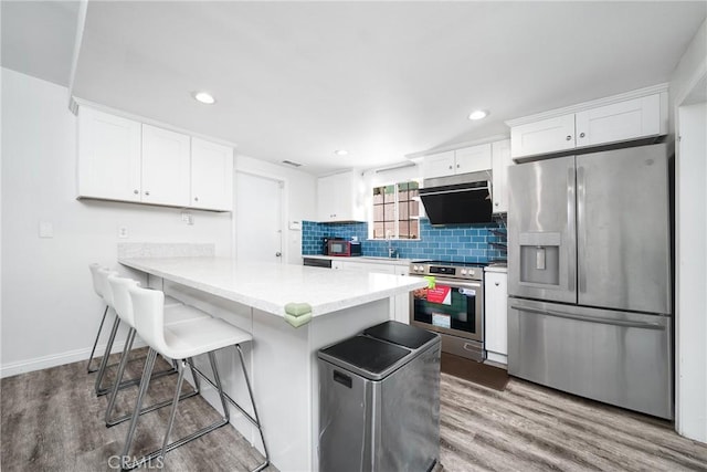 kitchen with stainless steel appliances, wood finished floors, white cabinetry, tasteful backsplash, and a kitchen bar