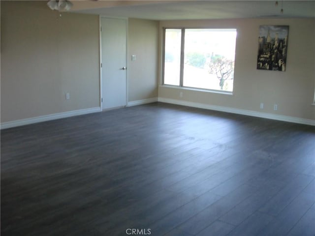 spare room with dark wood-style flooring, a ceiling fan, and baseboards