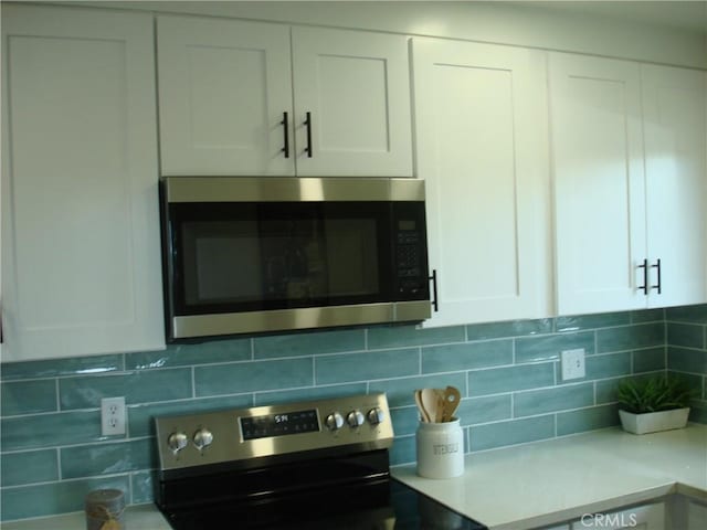 room details featuring stainless steel appliances, tasteful backsplash, light countertops, and white cabinetry