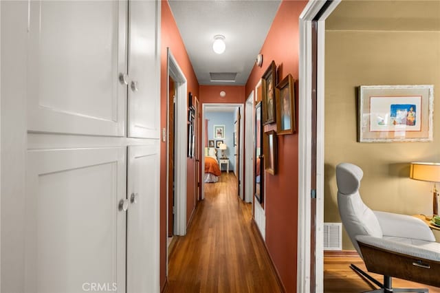 hall featuring wood finished floors, visible vents, and attic access