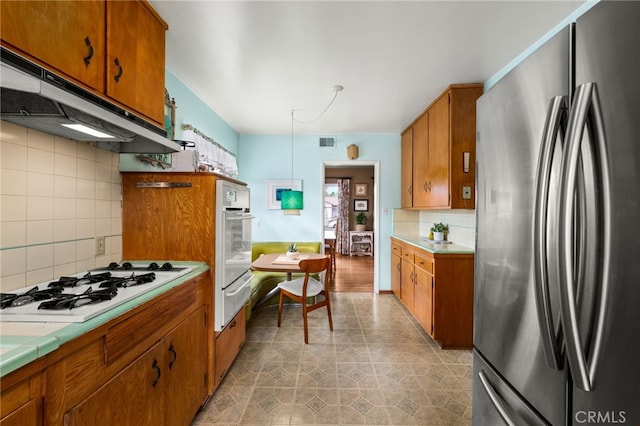 kitchen featuring tasteful backsplash, visible vents, brown cabinetry, white appliances, and under cabinet range hood