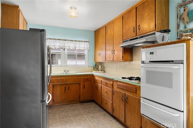 kitchen with white appliances, light countertops, under cabinet range hood, backsplash, and a warming drawer