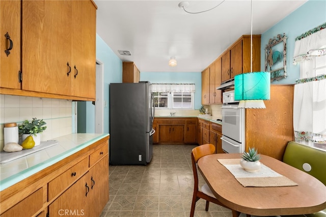 kitchen with tile countertops, visible vents, backsplash, brown cabinetry, and freestanding refrigerator