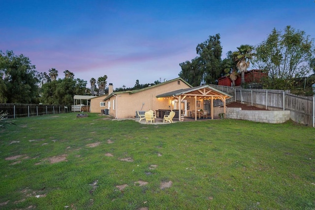 back of house at dusk with a patio area, a lawn, a fenced backyard, and stucco siding