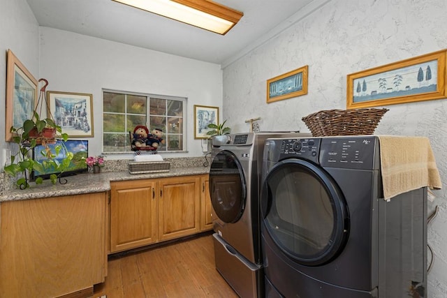 washroom featuring cabinet space, washing machine and dryer, and light wood finished floors