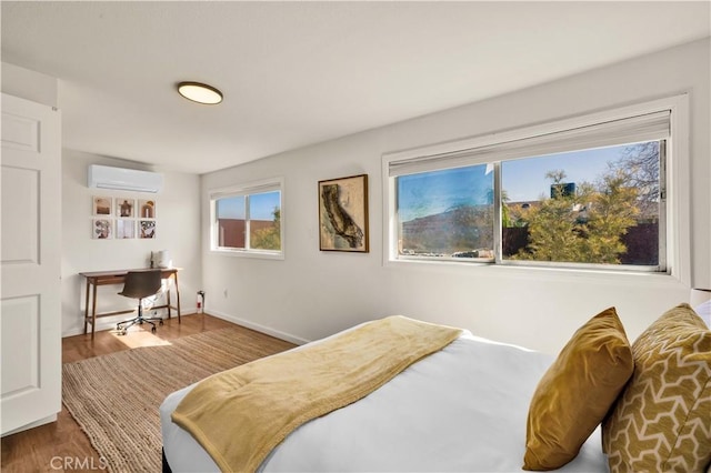 bedroom featuring a wall unit AC, baseboards, and wood finished floors