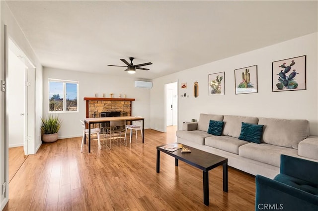 living area with a wall unit AC, a fireplace, ceiling fan, light wood-type flooring, and baseboards