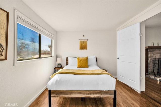 bedroom with a fireplace with raised hearth, baseboards, and wood finished floors