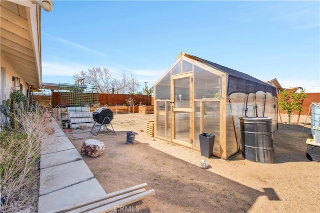 exterior space with a greenhouse, a fenced backyard, a patio, and an outbuilding