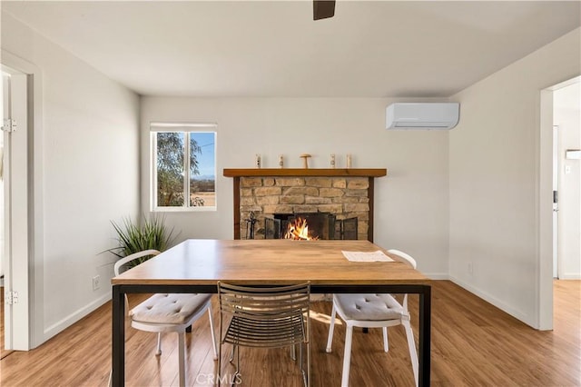 office space featuring light wood-style flooring, a wall mounted air conditioner, a stone fireplace, and baseboards