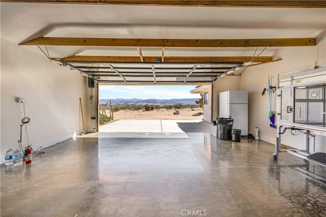 garage with freestanding refrigerator, a mountain view, and baseboards