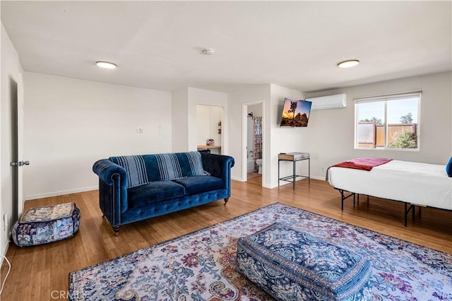 bedroom with a wall unit AC, wood finished floors, and baseboards