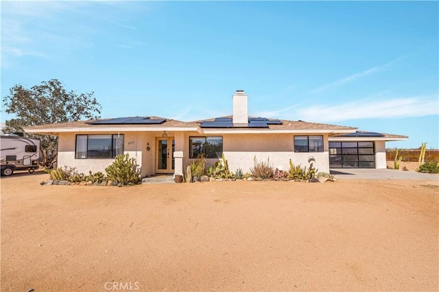 view of front of property with a garage, driveway, roof mounted solar panels, a chimney, and stucco siding