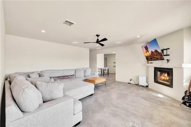 living room featuring finished concrete flooring, visible vents, a glass covered fireplace, ceiling fan, and recessed lighting