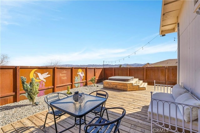 wooden terrace featuring outdoor dining area, a fenced backyard, hot tub deck surround, and a mountain view