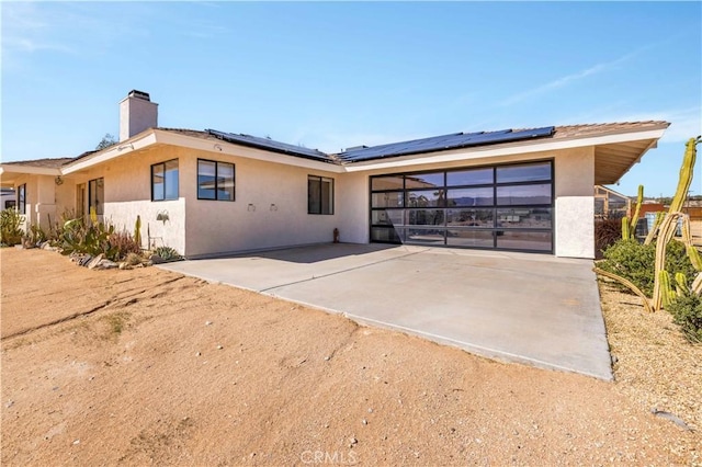 view of front facade featuring roof mounted solar panels, a chimney, and stucco siding