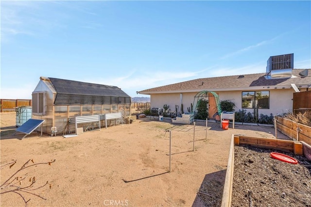 back of property with a greenhouse, an outbuilding, stucco siding, cooling unit, and a garden