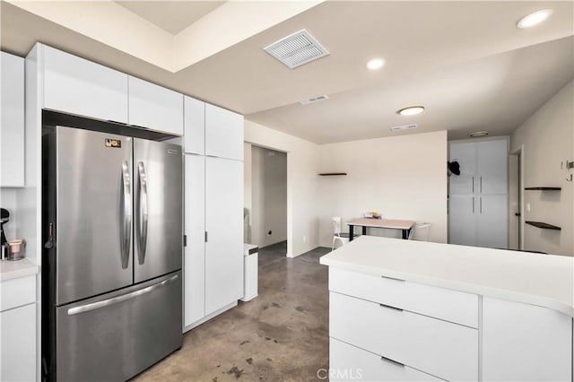 kitchen with visible vents, white cabinets, freestanding refrigerator, light countertops, and concrete floors