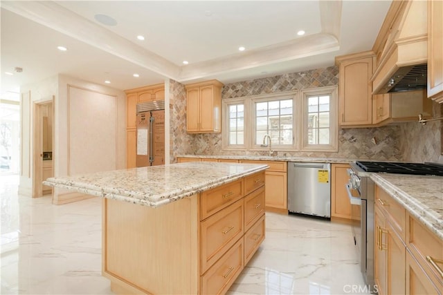 kitchen with marble finish floor, high quality appliances, a tray ceiling, and light brown cabinetry