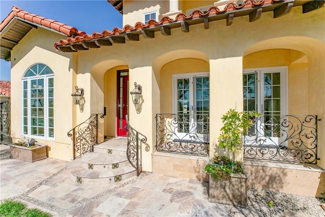 entrance to property featuring a patio, a tile roof, and stucco siding