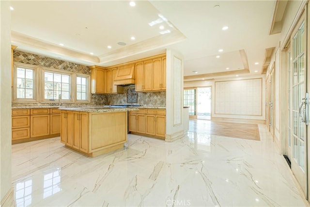 kitchen featuring a healthy amount of sunlight, marble finish floor, a tray ceiling, and a center island