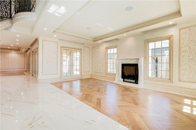 unfurnished living room featuring french doors, a raised ceiling, ornamental molding, a high end fireplace, and wallpapered walls