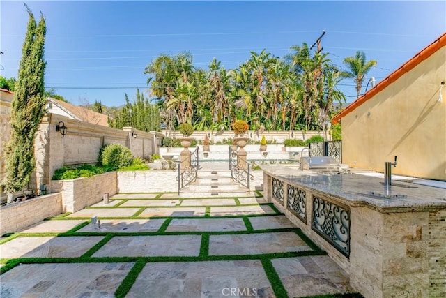 view of patio with exterior kitchen, a fenced backyard, and a grill