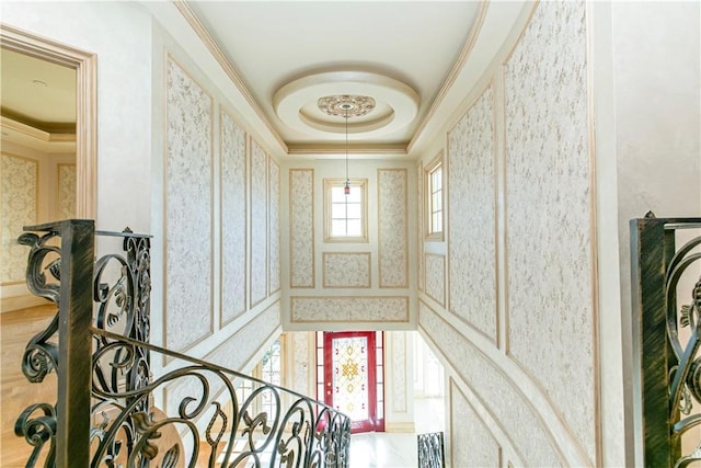 stairway with ornamental molding, a tray ceiling, and wallpapered walls