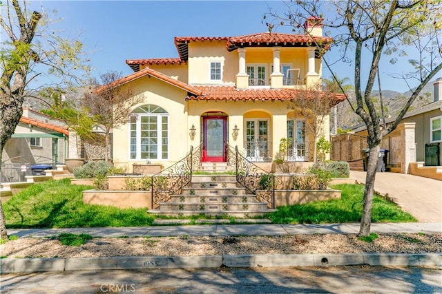 mediterranean / spanish-style home featuring french doors, a chimney, stucco siding, a balcony, and a tiled roof