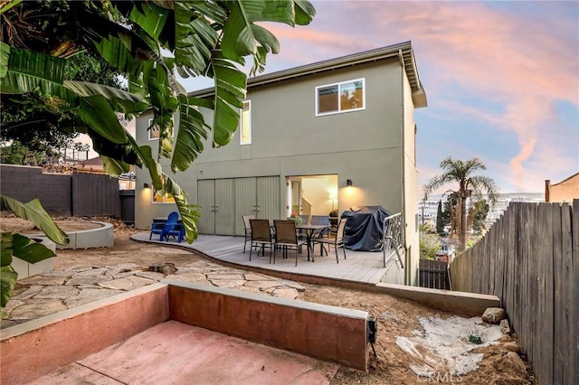 back of house at dusk with stucco siding, a fenced backyard, and a wooden deck