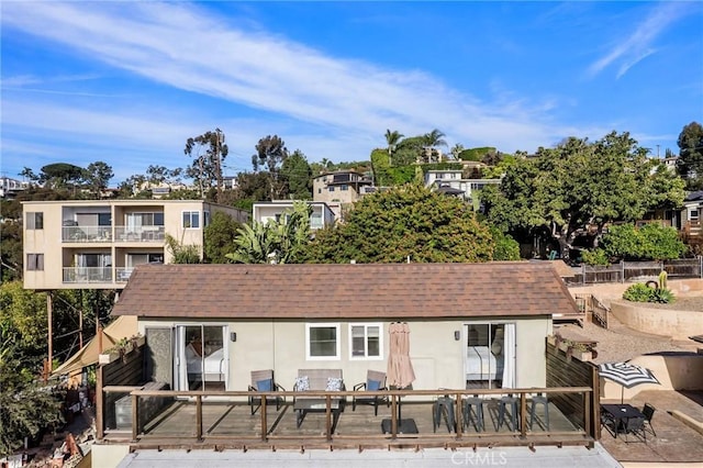 back of property with a shingled roof, fence, and stucco siding