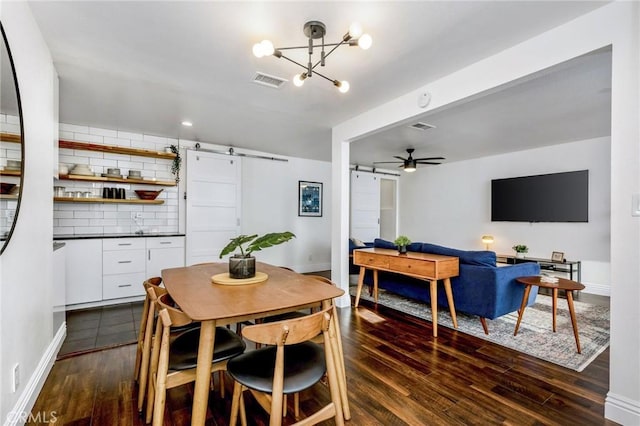 dining room featuring visible vents, a barn door, dark wood-type flooring, baseboards, and ceiling fan with notable chandelier