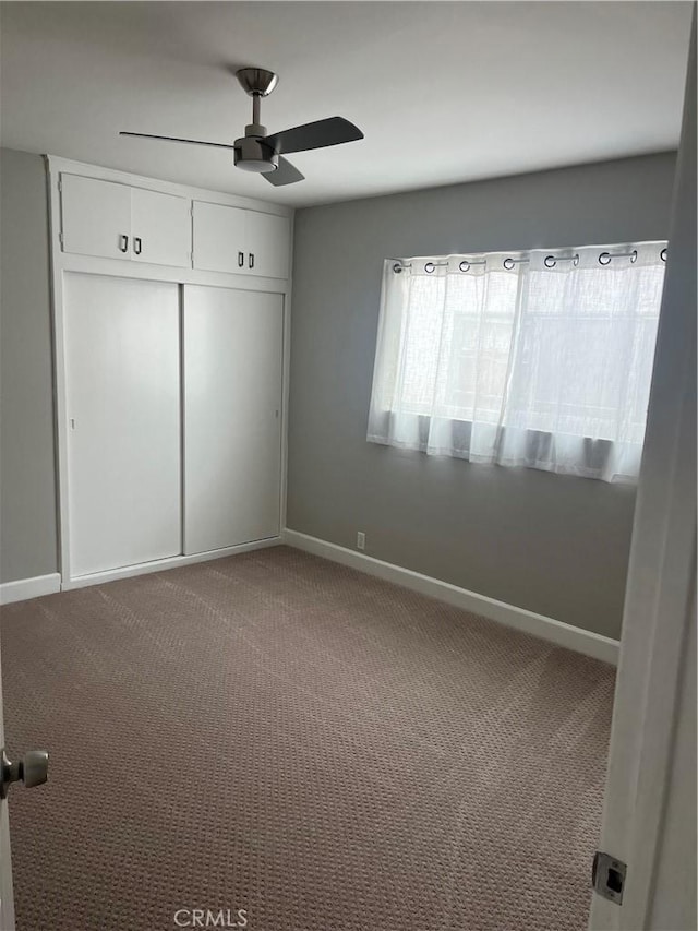 unfurnished bedroom featuring carpet floors, a closet, baseboards, and a ceiling fan