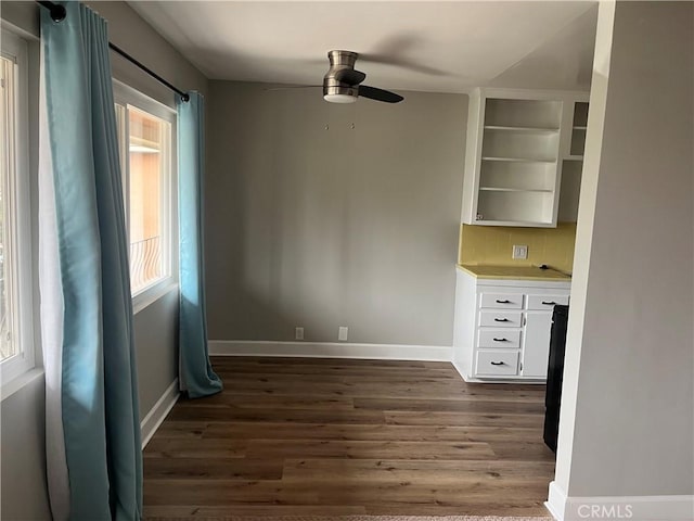 unfurnished dining area with dark wood-style floors, ceiling fan, and baseboards