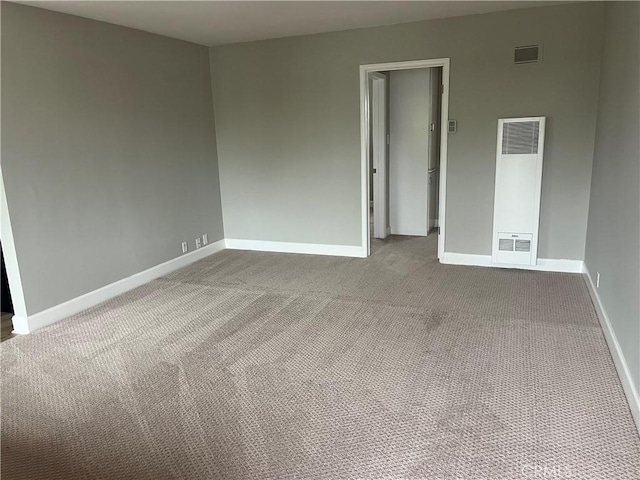 empty room featuring a heating unit, carpet, visible vents, and baseboards